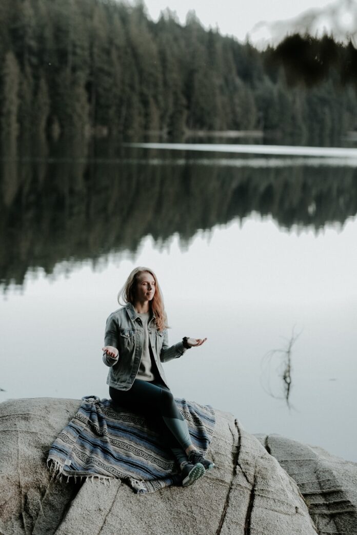 Photo by Priscilla Du Preez 🇨🇦 woman meditating on rock in bank of lake