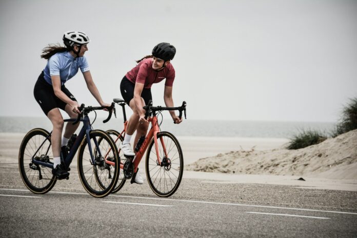 Photo by Coen van de Broek man and woman riding road bikes at the road near shore