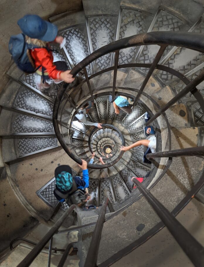 Photo by Howard Walsh a group of people climbing up a spiral staircase